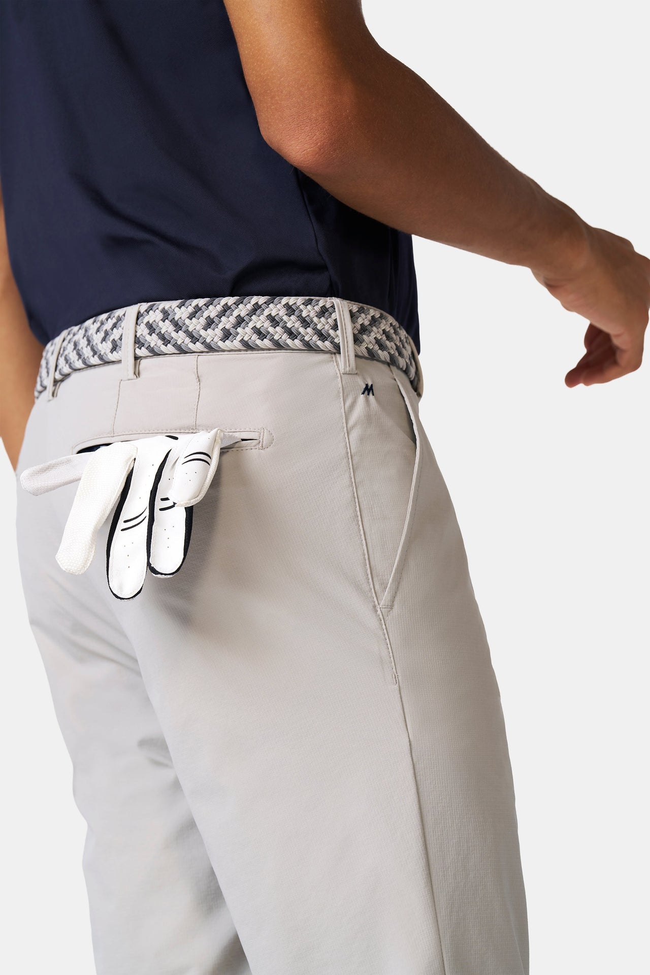Person wearing light gray pants with a patterned belt and white golf glove.